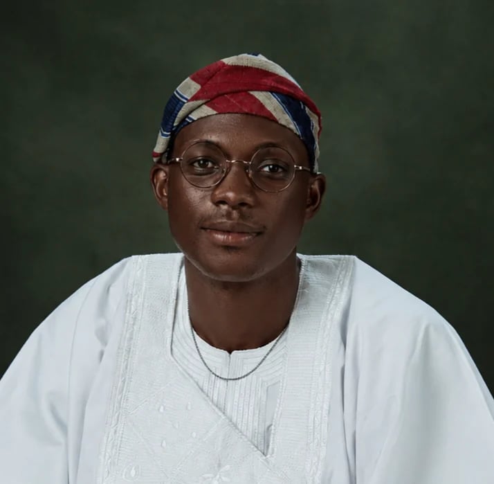 Portrait of a man wearing glasses, a red and white patterned headwrap, and a white textured shirt against a green background