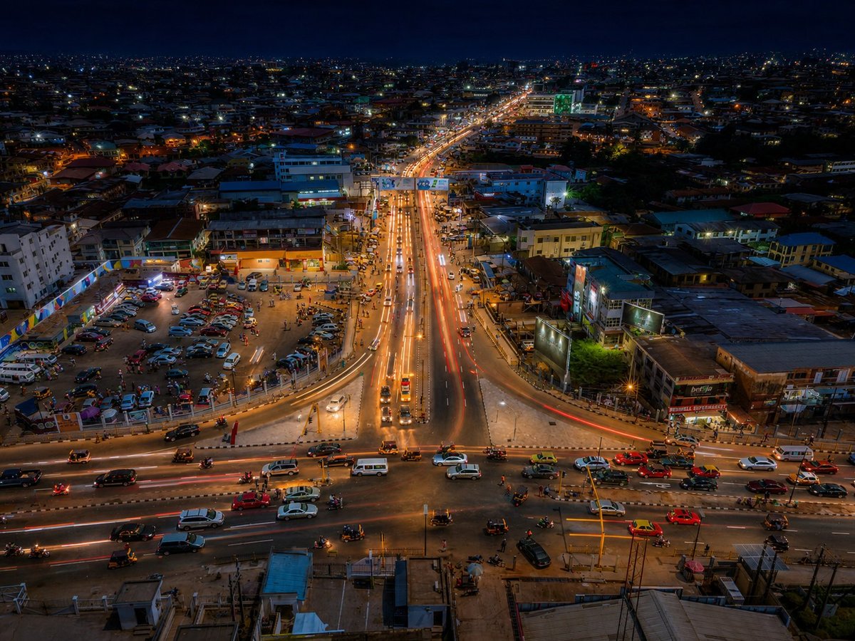 Elevated nighttime view of a busy multi-lane highway interchange with illuminated roads and traffic in an urban cityscape.