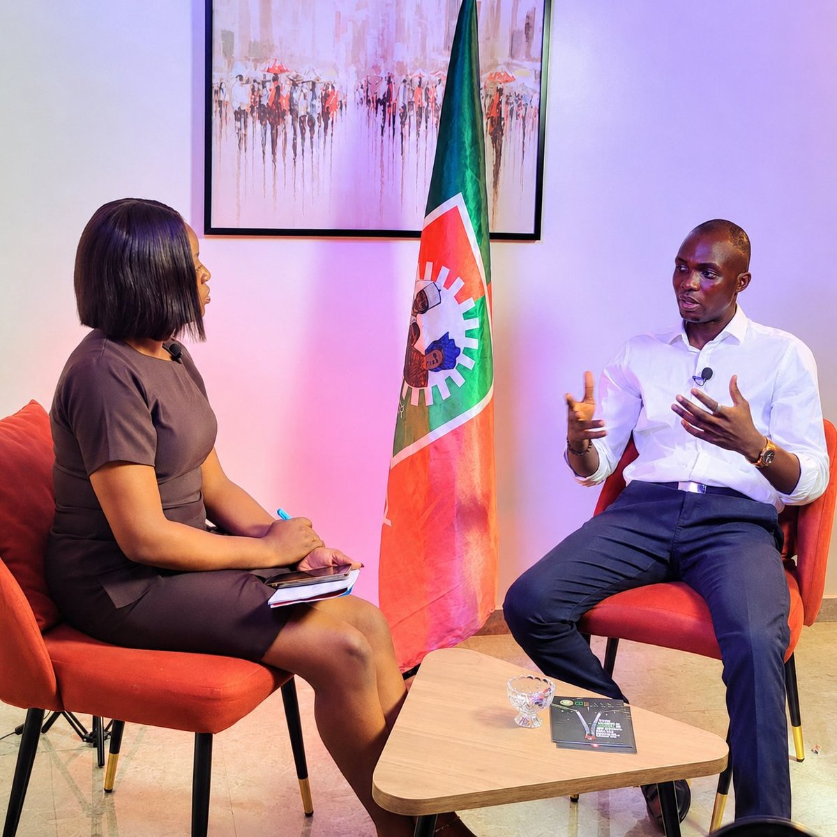 Two professionals having a conversation in a studio setting with a colorful flag and abstract artwork in the background